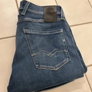 Replay Anbass Hyperflex jeans blå - Snygga Replay Anbass Hyperflex jeans i klassisk blå tvätt. Modellen har fem fickor, normal passform och raka ben. Jeansen är tillverkade i stretchigt denim. Säljer för jag upplevde dom långa i storleken har L30 men skulle säga att de passar L31 och L32 bättre på mig blev dom långa. Är inte använda mer än 1 gång. 1 799kr orginalpris säljer för 950 men kan diskuteras.