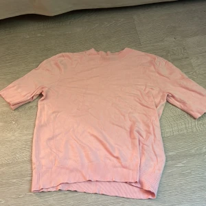 Ljusrosa stickad tröja 157 M - Supersöt ljusrosa stickad tröja från 157 med ribbade muddar och kortare ärmar. Perfekt för dig som gillar en enkel men ändå trendig look. Mjuk och skön, passar till både jeans och kjol.