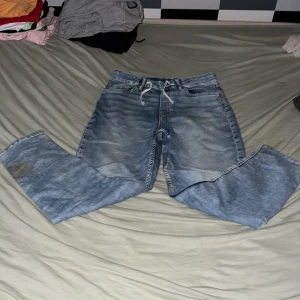 Blå tapered jeans från H&M - Snygga ljusblå jeans från H&M med relaxed fit och tapered ben. Jeansen har justerbar midja med snörning och klassisk femficksdesign. Perfekta för en chill och avslappnad stil.