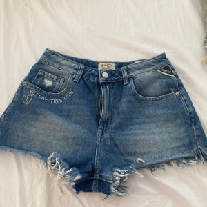 Blå jeansshorts från Replay - Jätte fina jeansshorts från Replay, från deras ”Reply True Love” kollektion. Den kommer vara perfekt nu till kvällspromenader under sommaren. Den är i storlek 26 men passar mig perfekt som är 24, använd fåtal gånger. Priset kan diskuteras, fråga gärna om fler bilder!!