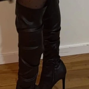 Svarta höga stövlar med klack - Snygga svarta stövlar i skinnimitation med hög klack och spetsig tå. Stövlarna går över knäet och har en elegant, slät finish som ger en stilren look. Perfekta för att lyfta vilken outfit som helst. Köpt från new yorker för 499kr. Endast använd i två timmar