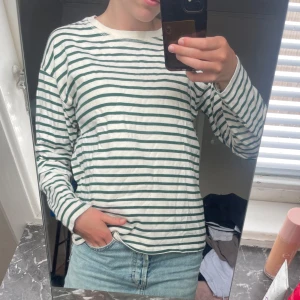 Randig långärmad tröja från Zara - Säljer en vit långärmad tröja från Zara med gröna horisontella ränder. Tröjan har en klassisk rund halsringning och är gjord i mjuk bomull. Använd fåtal gånger💞💞