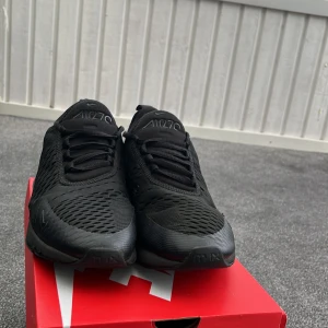 Nike Air Max 270 Triple Black 42,5 - Nike Air Max 270 i helsvart färg med mesh-ovandel och synlig Air-enhet i hälen. Snygg sportig look med diskreta loggor och snörning. Perfekta sneakers för dig som gillar stilrena och bekväma skor med modern vibe. Sko låda ingår ej.