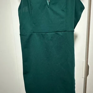 Mörkgrön ärmlös klänning - Snygg mörkgrön klänning med enkel och stilren design. Klänningen är ärmlös och har en rak passform med en liten v-ringning framtill. Perfekt för dig som gillar minimalistisk stil och vill ha något som sticker ut med sin djupa gröna färg. Den är thight på!