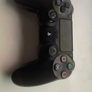 PS4 Kontroll - Bilderna visar en svart PlayStation-handkontroll, troligen till PS4. Den har tydliga tecken på användning, särskilt på baksidan där etiketten är sliten. Perfekt för dig som vill ha en extra kontroll till gamingkvällar med vänner.