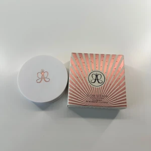 Anastasia Glow Seeker Highlighter - Glow Seeker Highlighter i nyansen Sun Idol från Anastasia Beverly Hills. Kommer i en rund vit dosa med spegel och roségulddetaljer. Ger en intensiv, guldig glow med skimrande finish. Förpackningen har snyggt rosa och vitt mönster med logga.  Kommer med original förpackningen. Använt några få gånger som ni ser. 