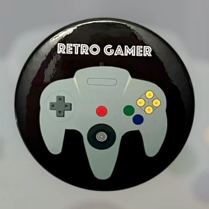 Retro Gamer Pin Nintendo 64 Badge - En snygg pin med en N64 handkontroll och texten RETRO GAMER. Ca 4,4 cm i diameter. Perfekt för den som älskar Nintendo och gamla tv-spel! 