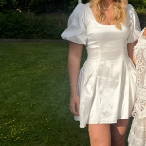 Vit kort klänning med puffärm NA-KD - Vit kort klänning från NA-KD med puffiga korta ärmar och lite glansig i tyget. Beställde två olika storlekar och använde den ena på min student. Därav säljer jag den oanvända med prislapp kvar. Köpte för 650, säljer för 500.