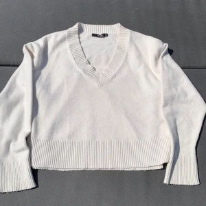 Vit stickad v-ringad tröja - Vit stickad tröja från Bik Bok med v-ringning och breda ribbade muddar vid ärmslut och nederkant. Tröjan har en avslappnad passform och är perfekt för lager-på-lager-stil. Enkel att matcha med både jeans och kjol.