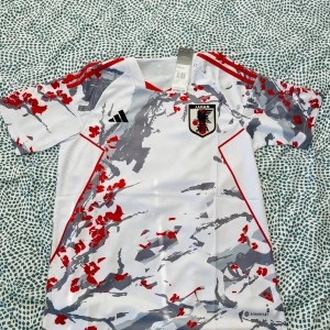 Japan fotbollströja Adidas vit/röd - Japan landslagets fotbollströja från Adidas i vitt med grått och rött kamouflagemönster. Tröjan har korta ärmar, röda detaljer på axlarna och klubbmärke på bröstet. Tillverkad i lätt och ventilerande material med Aeroready-teknologi.