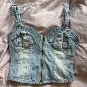  Guess jeanskorsett - Säljer denna snygga ljusblåa vintage korsettopp från guess i jeans med justerbara axelband, dragkedja framtill och cool snörning i ryggen. 