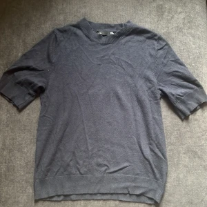 Mörkblå stickad tröja 157 XS - En stilren mörkblå stickad tröja från 157 i storlek XS. Tröjan har ribbade muddar vid hals, ärmslut och nederkant samt korta ärmar. Perfekt för lager-på-lager och funkar året runt. Enkel och clean design som passar till det mesta.