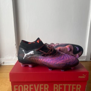 Elite Puma Fuzionfit+ lila/svarta fotbollsskor - Snygga Puma Fuzionfit+ fotbollsskor i svart och lila med coola röda detaljer och mönstrad ovandel. Skorna har snörning, strumpliknande skaft och en yttersula med lila och rosa dobbar för grymt grepp på planen. Perfekta för dig som vill sticka ut på matchen.