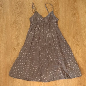 Brunprickig sommarklänning från H&M stl. 36 - brun kortklänning från H&M med vita prickar och tunna justerbara axelband. Klänningen har v-ringad urringning med rynkdetalj framtill och ett luftigt, volangigt fall.