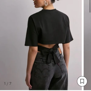 Nelly tie back top - Snygg svart topp med korta ärmar och cool knytning i ryggen. Toppen har en enkel, stilren look framifrån och en öppen rygg med breda band som knyts till en rosett. Perfekt för dig som gillar trendiga detaljer och vill sticka ut.