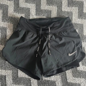Svarta Nike Dri-FIT träningsshorts XS - Svarta Nike Dri-FIT shorts med snörning i midjan och liten dragkedjeficka bak. Lätta och snabbtorkande, perfekta för löpning eller gym. Snygg sportig look med Nike logga framtill och bekväm passform då det finns shorts invändigt också. Använda max 2 gånger, säljer nu pga att de inte är min storlek längre.🏃‍♀️🎽