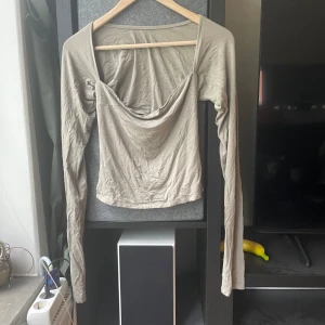 Khaki långärmad topp Gina Tricot - Säljer en beige långärmad topp från Gina Tricot med snygg draperad urringning och croppad passform. Tunt och mjukt material som känns skönt mot huden. 