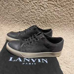 Svarta sneakers från Lanvin  - Stilrena svarta sneakers från Lanvin med ovandel i mocka och detaljer i skinn. Skorna är stora i storleken och passar därför ca 42,5 Skorna har rund tå, snörning och vit platt sula. Perfekta för dig som gillar en clean och lyxig look med premiumkänsla. Priset ej  hugget i sten.                                                                           Medföljer gör original dustbag från Lanvin.                             Tveka inte att höra av dig om du har frågor eller vill ha fler bilder🤗