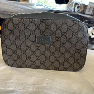 Gucci axelväska i grått GG-mönster - Snygg axelväska från Gucci i grått med klassiskt GG-mönster över hela väskan. Väskan har silverfärgad dragkedja och detaljer i skinn. Perfekt storlek för det viktigaste och en stilren look med exklusiv känsla.