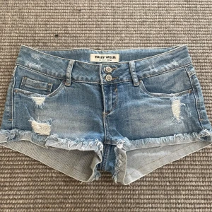 Super low rise ripped jeanshorts - Snygga blå jeansshorts från Tally Weijl med slitna detaljer och fransad kant. Modellen är lågmidjad med dubbla knappar framtill och klassiska fickor både fram och bak. Perfekta för sommaren och ger en cool, avslappnad vibe. Lågmidjade
