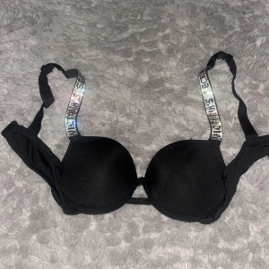 Svart bh från Victoria's Secret - Supersnygg svart bh från Victoria's Secret med glittriga axelband som verkligen sticker ut. Kuporna är vadderade och ger en snygg form. Helt ny använd kanske 1 gång.