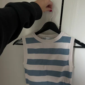 Randig ärmlös topp från Zara - Superfin ärmlös topp från Zara med breda blå och vita ränder. Toppen har rund halsringning och är stickad i mjukt material, perfekt för en fräsch och chill look. Passar snyggt till både jeans och kjol.