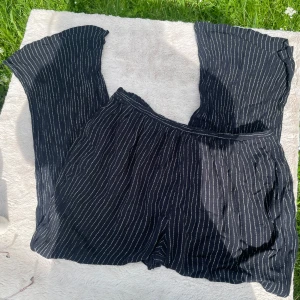 Randiga vida byxor från Maharani - Snygga svarta byxor med vita ränder från Maharani. De har en loose och wide passform med elastisk midja och är tillverkade i ett lätt och luftigt tyg, perfekt för varma dagar. Byxorna har en avslappnad vibe och passar dig som gillar bekväma och trendiga plagg