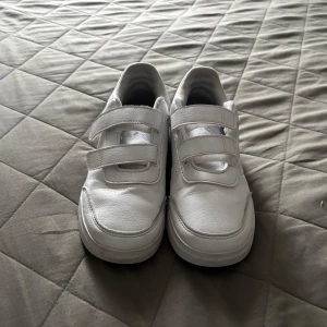 Vita adidas sneakers med kardborre - Fräscha vita sneakers från adidas med klassiska tre ränder på sidan. Skorna har två breda kardborreband för enkel påtagning och en platt sula. Skriv för fler frågor eller bilder i chatten tack!