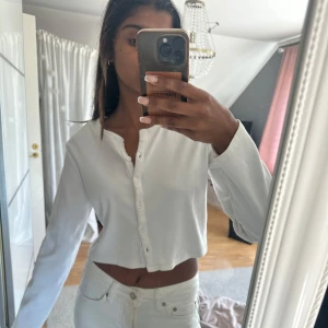 Vit croppad kofta från Zara - Säljer en vit croppad kofta från Zara med långa ärmar och ribbad struktur. Tröjan har knappar framtill. Storlek L men passar mig perfekt som vanligtvis har S, använd fåtal gånger! 