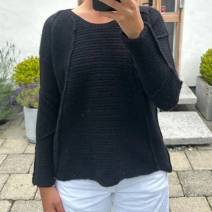 Svart stickad tröja med struktur - En svart stickad tröja med rund hals och lång ärm. Tröjan har en lätt loose passform och synliga sömmar som ger en cool struktur. Perfekt att slänga på sig när det är kyligt ute. Enkel och stilren design som funkar till det mesta.