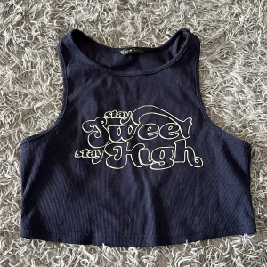 Mörkblå croppad linne från SHEIN - Croppad mörkblå linne från SHEIN med trycket 'stay sweet stay high' i vit retrostil. Ribbad struktur och ärmlös modell med hög halsringning. Tillverkad i stretchig polyesterblandning som sitter snyggt och bekvämt.