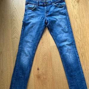 Slim Glenn blå jeans, storlek 31/34 - Snygga blå jeans från Slim Glenn i storlek 31/34. Modellen är slim fit med klassisk femficksdesign och lätt slitna detaljer framtill. Jeansen har normal midja och är tillverkade i mjukt denimtyg som sitter skönt hela dagen.