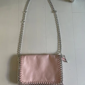 Rosa väska från Tiamo - Säljer en ljusrosa väska från Tiamo med silverfärgad kedja och detaljer längs kanterna❣️ kontakta gärna om ni har frågor eller prisförslag💗