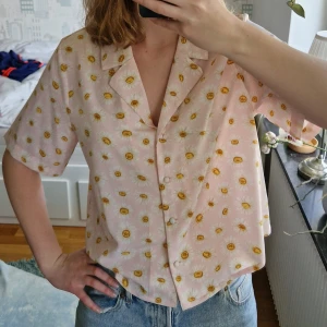 Kortärmad skjorta - Ljusrosa kortärmad skjorta med somrigt, blommigt mönster. Har "tygknappar" och är sydd uppe i ryggen baktill. Sparsamt använd och i gott skick!