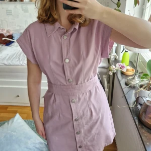Lila klänning - Skitsnygg lila, kortärmad klänning i jeansaktigt tyg och band för att knyta runt midjan. Knappar hela vägen och rätt vida axlar så är perfekt om man vill layera den. Oanvänd!