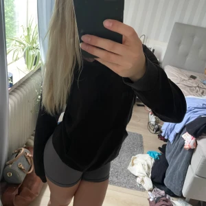 Svart hoodie i mjukt material - En svart hoodie med huva och långa ärmar. Tröjan har en klassisk passform och är tillverkad i ett mjukt, bekvämt material som passar perfekt för chill dagar eller när du vill ha en enkel och stilren look. Kommer från stadium och är i storlek XS.