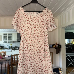Vit blommig kortklänning från SHEIN - Superfin vit kortklänning från SHEIN med röda små blommor och korta ärmar. Klänningen har en söt, lätt utställd passform och dragkedja i sidan. Perfekt för sommarens alla tillfällen och ger en romantisk vibe. Lite genomskinlig. Storlek L.  Aldrig använd. 