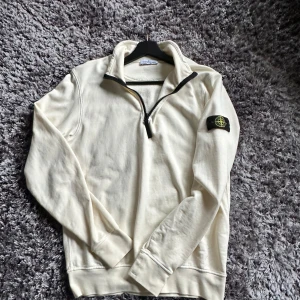 Vit half zip från Stone Island - Säljer en clean vit långärmad tröja från Stone Island med klassisk badge på ärmen. Tröjan har half zip-dragkedja och hög krage, perfekt för lager-på-lager. Tillverkad i mjuk bomull som känns skön mot huden. Enkel att matcha med jeans eller cargos.