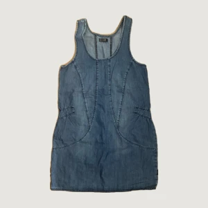 Jeansklänning från ONLY - Snygg ärmlös jeansklänning från ONLY i klassisk blå denim. Modellen är kort och har markerade sömmar samt två fickor i sidorna. Perfekt att styla med en t-shirt under eller som den är för en avslappnad look.