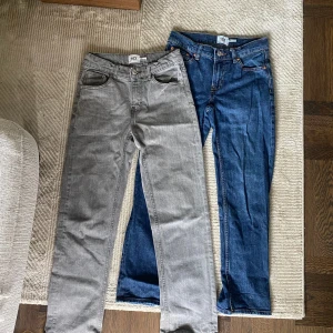 Två par jeans från 157, grå & blå - Säljer två par klassiska jeans från 157, ett par i grått och ett i blå denim. Båda har raka ben, fem fickor och knappgylf. Perfekta för dig som gillar enkel och tidlös stil. Materialet är tålig bomullsdenim och båda har justerbar midja på insidan.