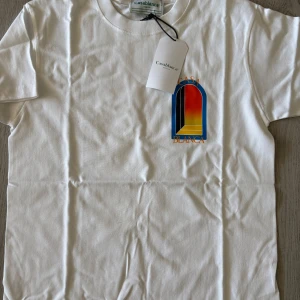 Vit t-shirt från Casablanca - Vit t-shirt från Casablanca med färgglatt tryck på bröstet i blått, rött och gult. Klassisk rund halsringning och korta ärmar. Tillverkad i mjuk bomull och har en clean vibe med snygg logga framtill.