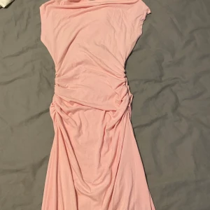 Ljusrosa långklänning med rynkade sidor - Supersöt ljusrosa långklänning i mjuk bomull med rynkade detaljer längs sidorna. Klänningen har en enkel rund halsringning och är ärmlös, vilket ger en avslappnad men ändå feminin look. Perfekt för varma dagar eller när du vill känna dig extra comfy.