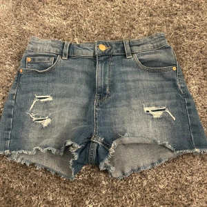 Blå jeansshorts med slitningar  - Snygga blå jeansshorts från Lindex med slitna detaljer framtill. Justerbart midjeband 