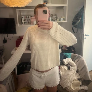 Vit stickad tröja med håldetaljer - Säljer en vit stickad tröja med rund hals och snygga håldetaljer längs ärmarna. Tröjan har en rak passform och långa ärmar, perfekt för lager-på-lager. Enkel och stilren design som funkar till många outfits.