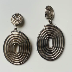 Stora spiralformade örhängen  - Unika statement-örhängen i spiralformad design, tillverkade i silverfärgad metall. Ovala och runda former med coolt, snurrat mönster och clip-on fäste. Ca 7 cm långa – perfekta för dig som vill sticka ut med en retrovibe.