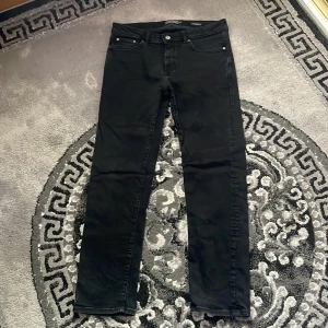  Dressmann jeans  - Svarta jeans från Dressmann i slim fit-modell. Klassisk femficksdesign med knapp och dragkedja framtill. Snygg, stilren look som passar till det mesta. Jeansen är tillverkade i ett stretchigt material för extra komfort.