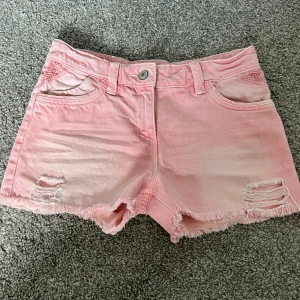 Rosa jeansshorts med slitningar - Snygga ljusrosa jeansshorts från Aeropostale med fransig kant och slitna detaljer framtill. Klassisk femficksmodell med bälteshällor och knappstängning. Perfekta för varma sommardagar och en avslappnad look. Jag säljer pga försmå. Skulle säga att de är i xs-s 