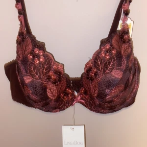 röd blommig bh från LingaDore - Helt ny.  Nypris 410kr      Supersnygg röd bh från LingaDore med broderade blommor och blad i rosa och rött. Bh:n har en liten rosett framtill och detaljerade axelband med broderade blommor. Perfekt för dig som gillar unika och romantiska underkläder.