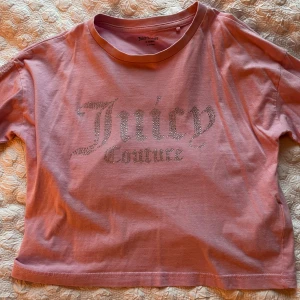 Rosa Juicy Couture t-shirt med strass - Superfin rosa t-shirt från Juicy Couture med glittrande strassdetaljer på bröstet och längs ärmarna. Croppad modell med klassisk rund halsringning. Perfekt för dig som vill sticka ut med en ikonisk och trendig look.