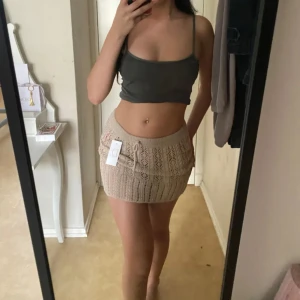 Beige stickad minikjol med snörning - Supersöt beige stickad minikjol med snyggt hålmönster och snörning i midjan. Kjolen har en tight passform och känns både trendig och cozy. Perfekt att styla med en croppad topp eller oversized hoodie för en chill vibe.